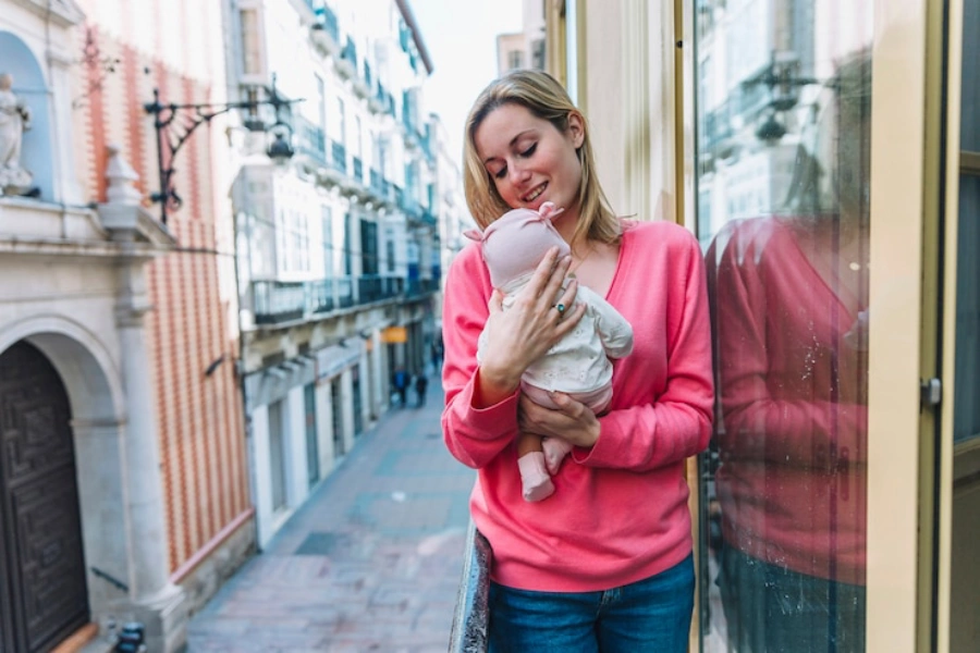 Mulher segurando bebe na sacada. Licença maternidade na Itália.